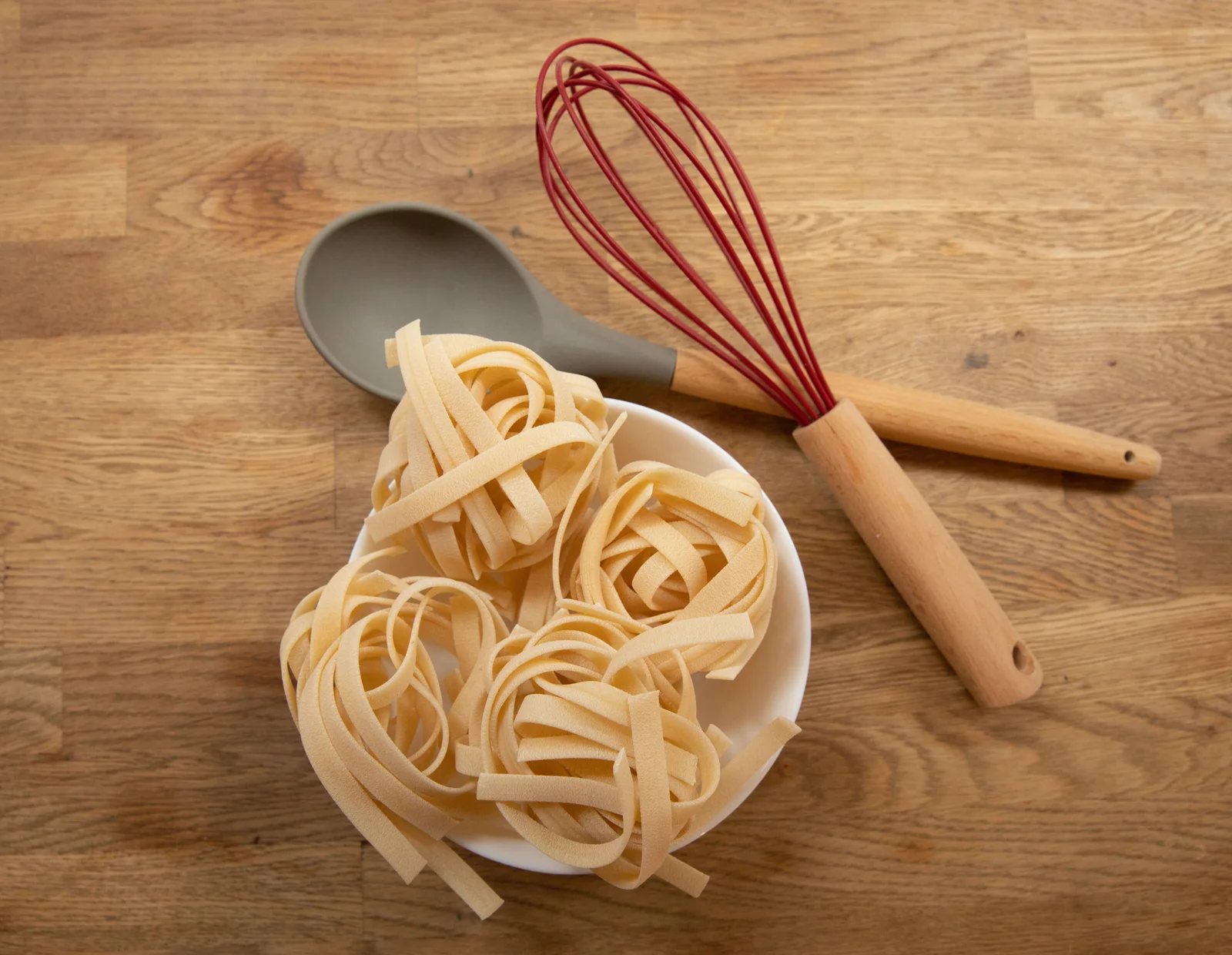 Uncooked tagliatelle nests in a bowl on a wooden preparation surface