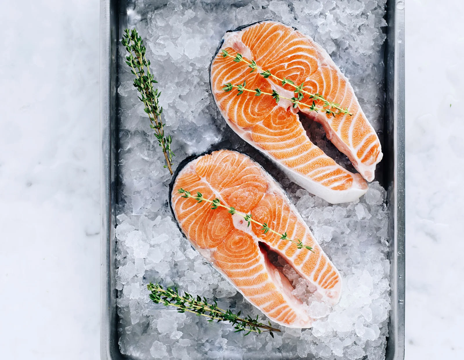 Raw salmon steaks with thyme on a tray of ice